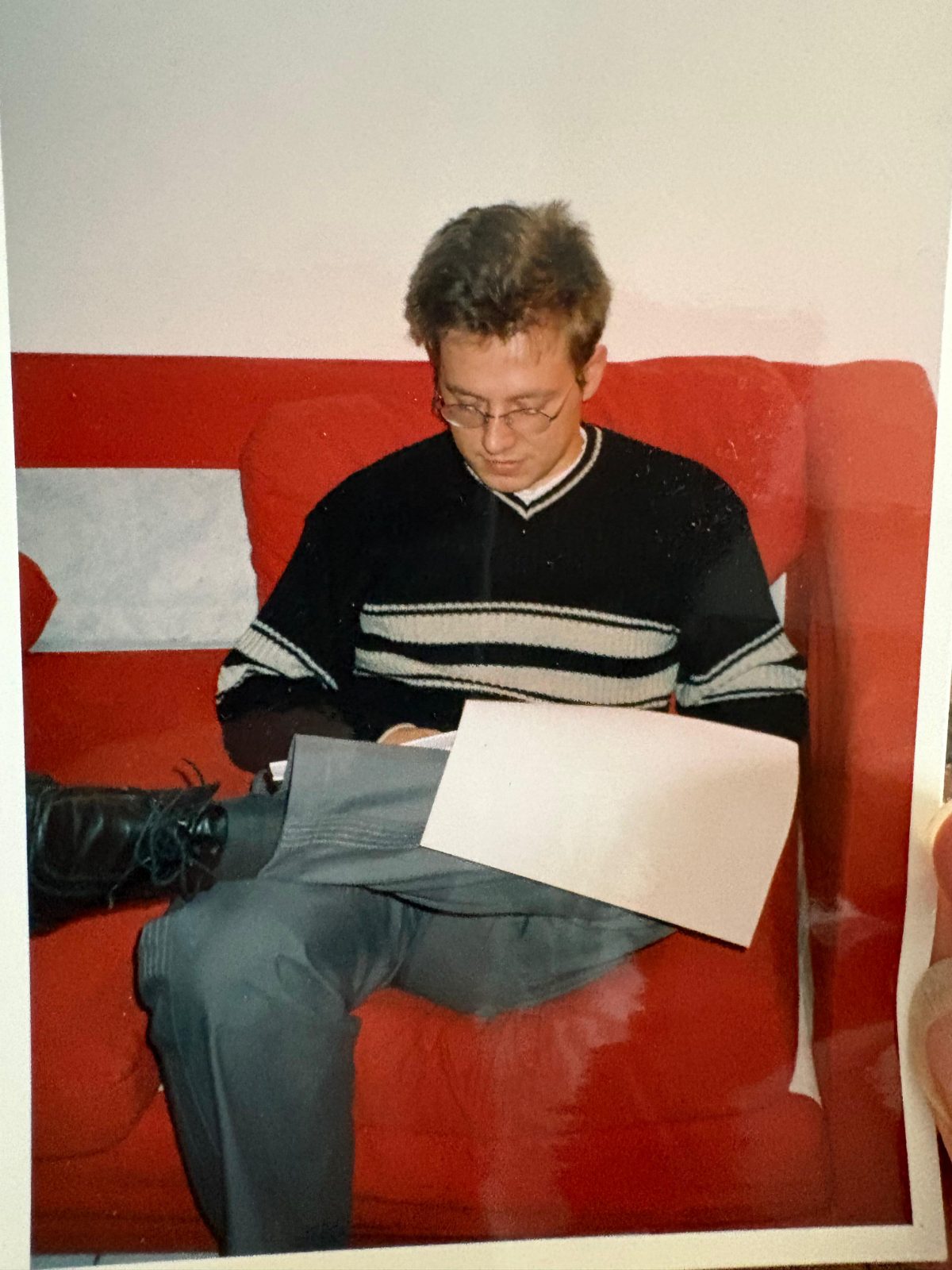 A print from the thesis years: Nicolas Boitout, in glasses and a
                          striped jumper, sitting on a red sofa and reading a sheet of paper
                          on his lap.